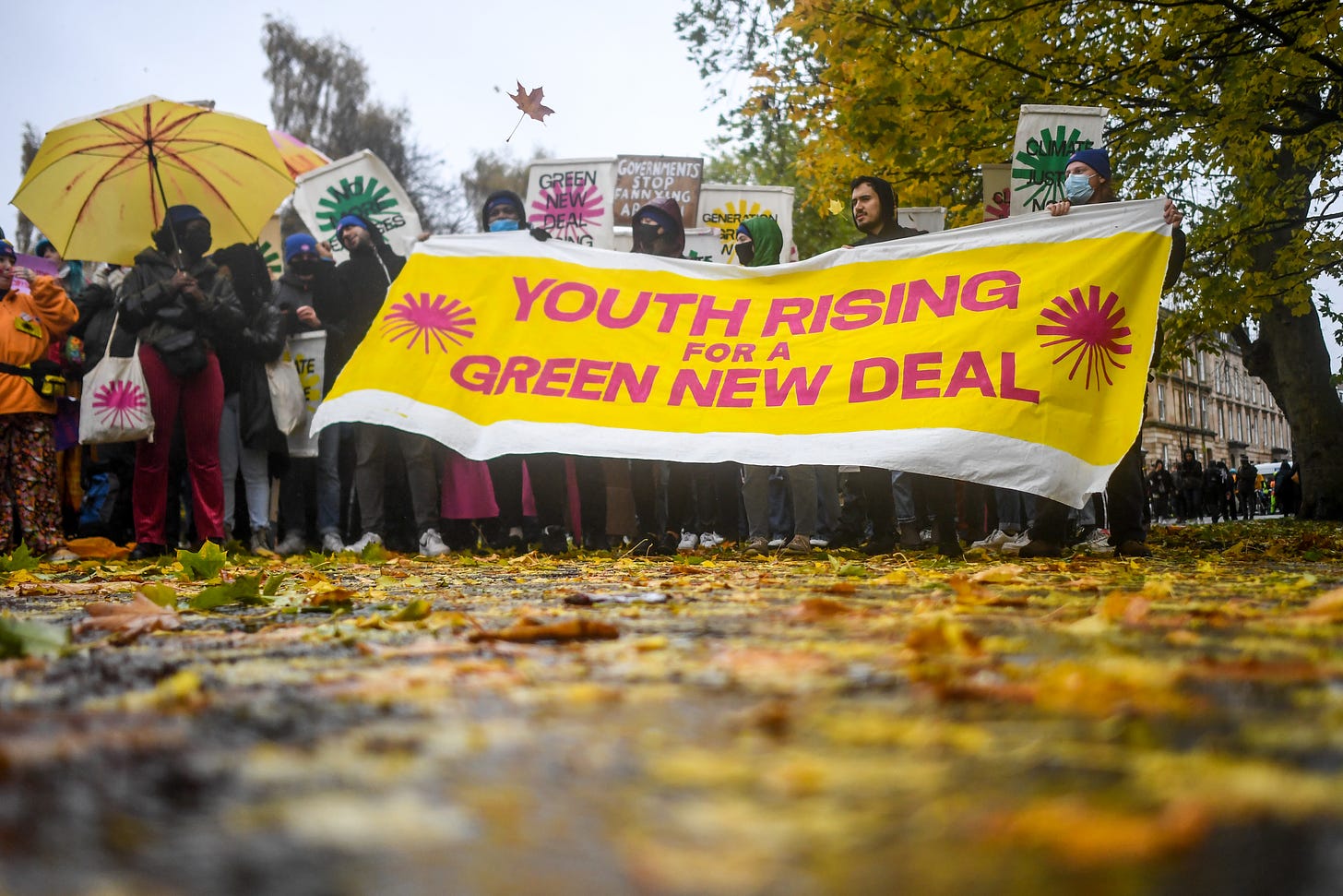 Photo of protestors in the rain in Glasgow holding a yellow banner that says 'Youth for Green New Deal'