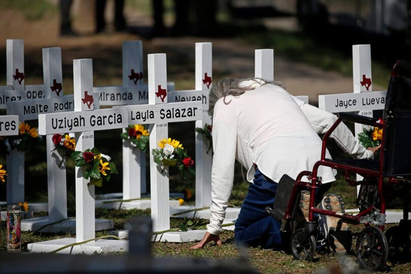 A woman kneels as she pays her respects in front of white crosses with the names of children killed, including colorful flowers at each cross, outside of the Robb Elementary School in Uvalde, Texas Thursday, May 26, 2022. 
