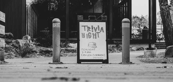 black and white scene with a sandwich board advertising trivia night