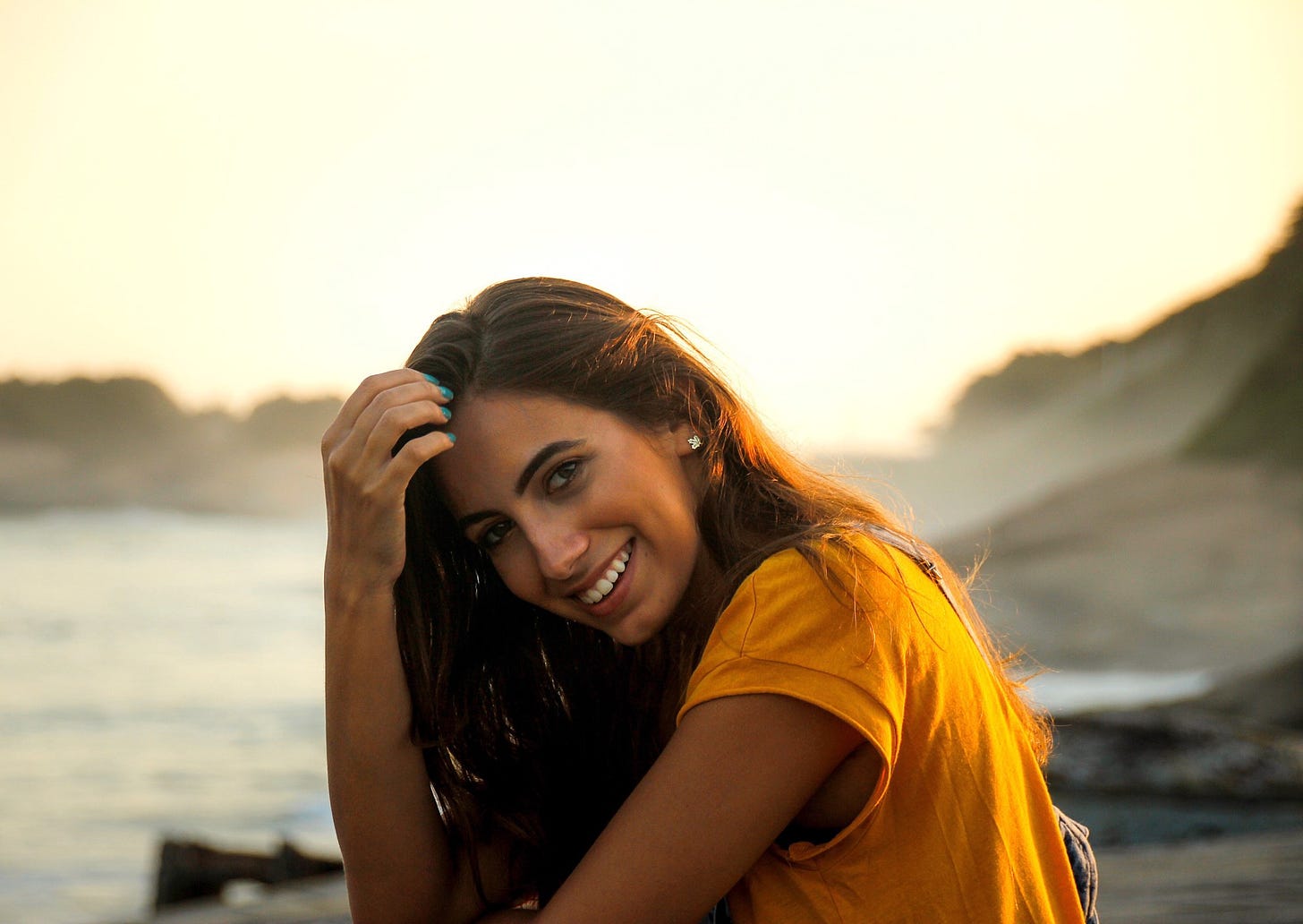 A woman with dark hair smiles at the camera. The sun sets over a beach behind her.