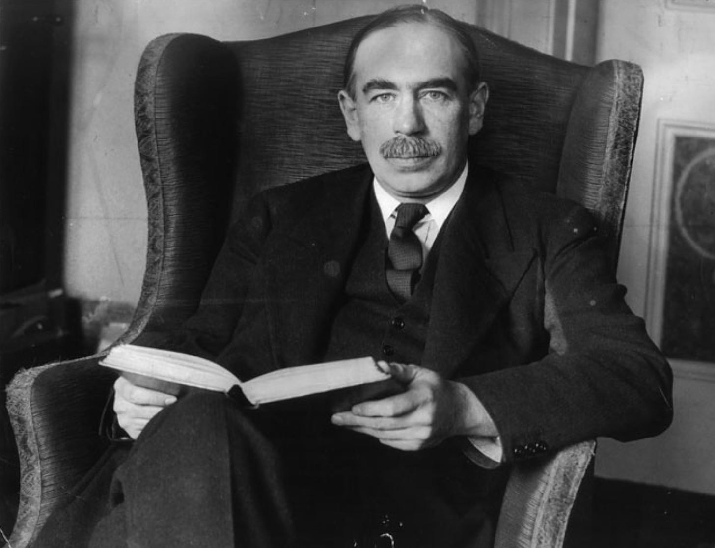 John Maynard Keynes gripping a book - black and white photo. He has a moustache and looks very serious!