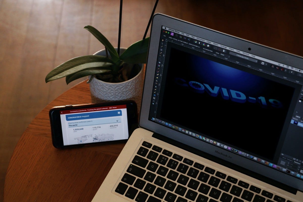 Laptop with Photoshop opened, COVID-19 text is across the screen. Phone with COVID news on the phone next to laptop.