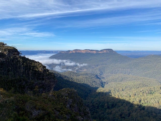 A view out into the valley and to the surround Blue Mountains, with low hanging clouds and a blue sky