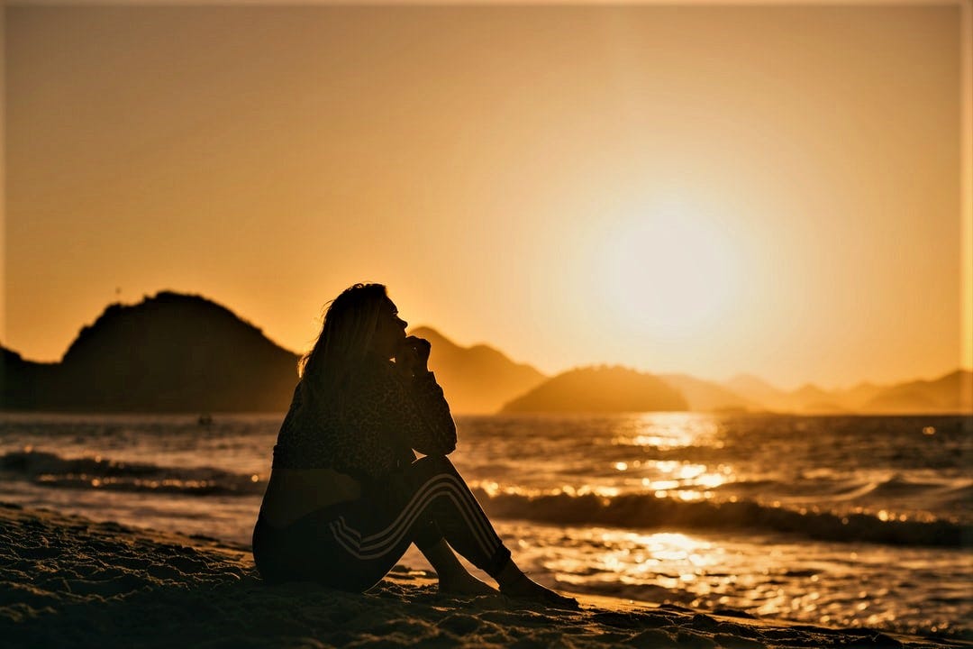 silhouette of woman sitting on beach looking out at the ocean at sunset silhouette of woman sitting on beach looking out at the ocean at sunset