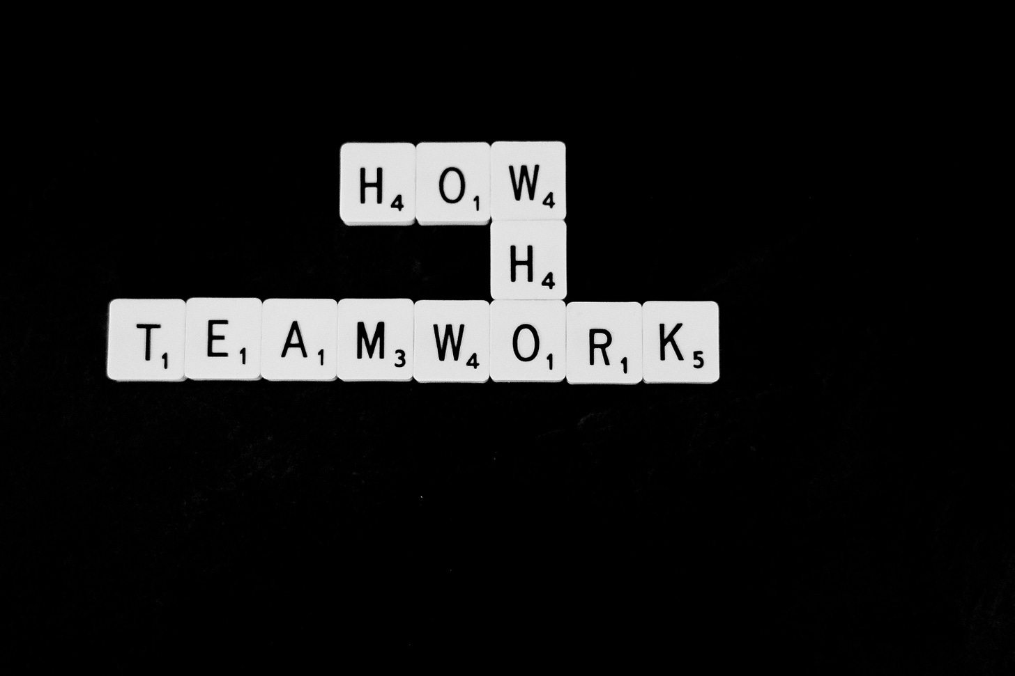 the words how who teamwork spelled out in scrabble letters on a black background