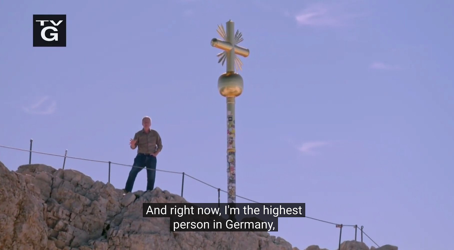 Rick Steves standing atop a mountain, proclaiming to be the highest person in Germany.