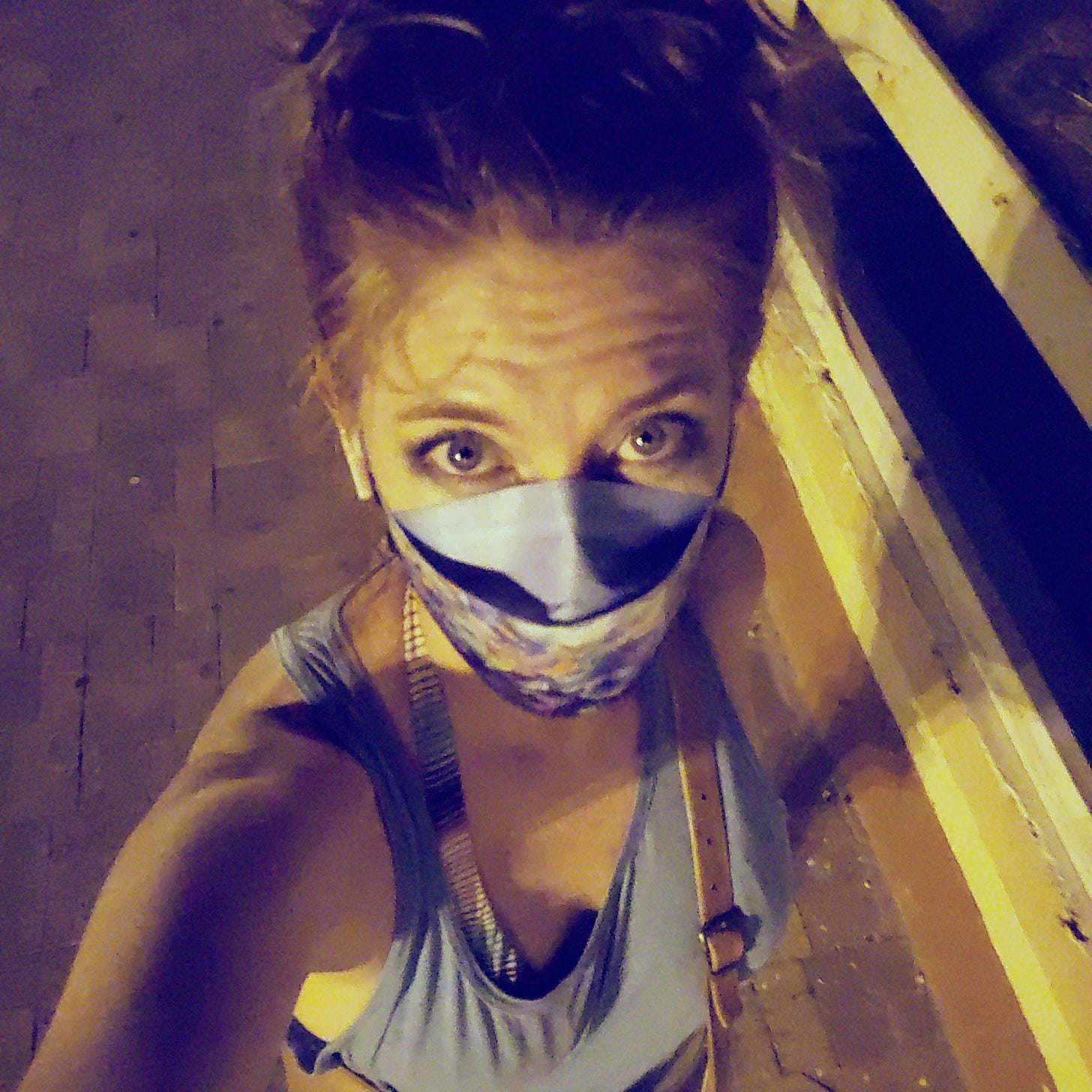 White woman in a mask and blue tank top staring up at the camera at night.  