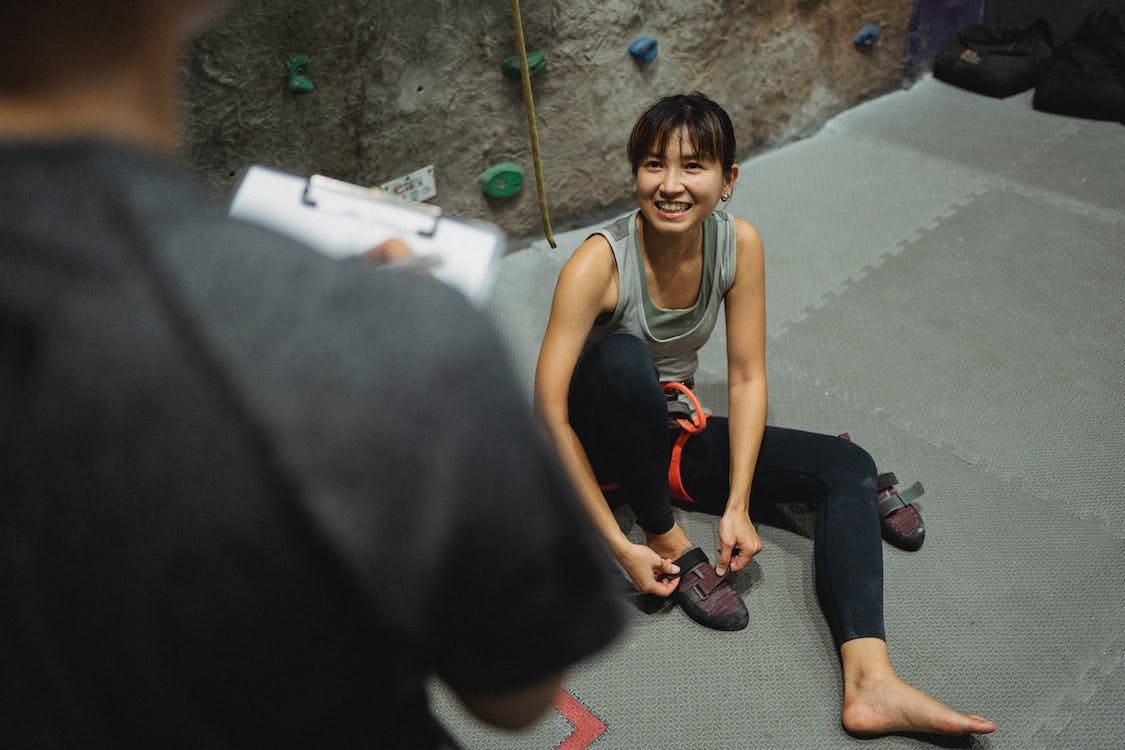 Free From above of cheerful ethnic female listen to coach while sitting on floor after climbing Stock Photo