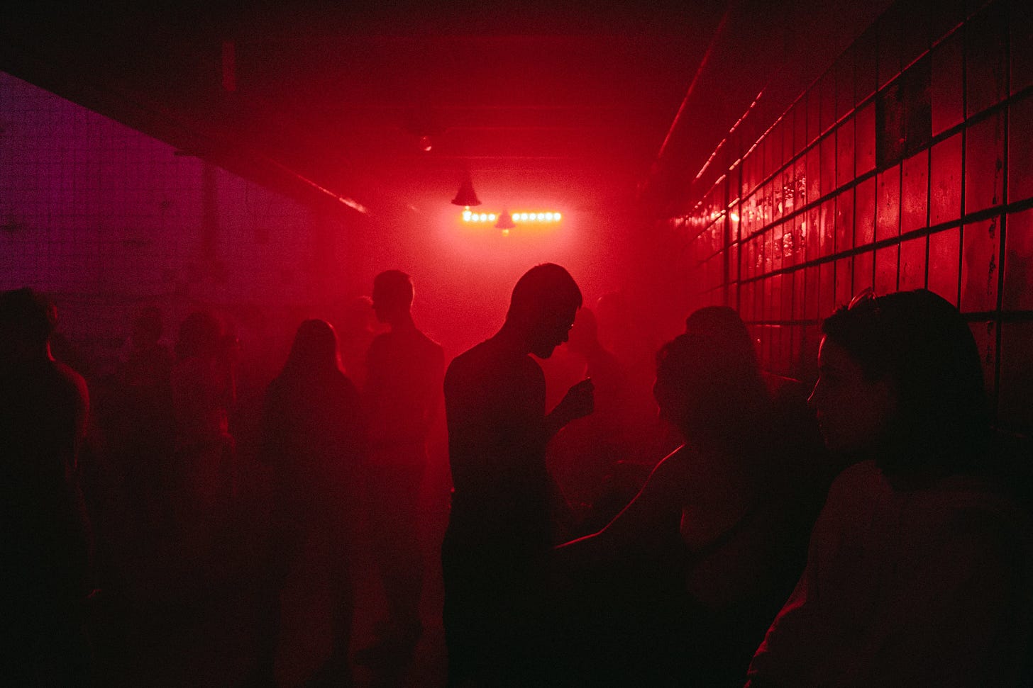 Picture of a cool, dimly-lit smoky club scene with people talking silhouetted in red.