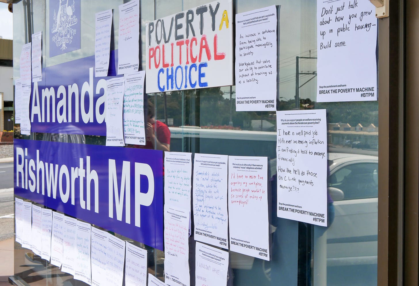 Photograph of a glass fronted office with large white lettering on a blue background that says "Amanda Rishworth MP". Posters and protests signs have been stuck to the glass. 