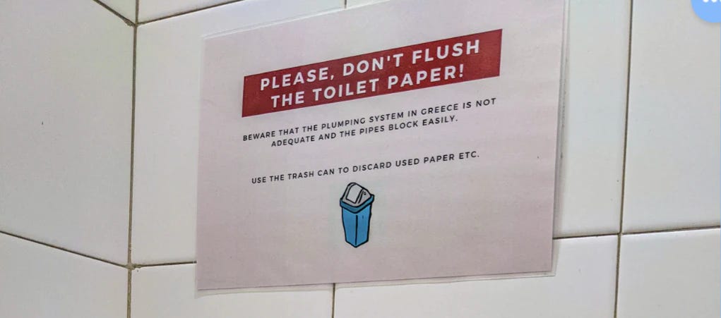 A sign in an Athen's bathroom warning people to not flush the toilet paper. 