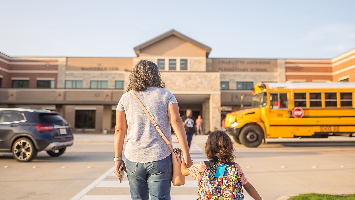 a family member walking through a crosswalk toward the school with a child