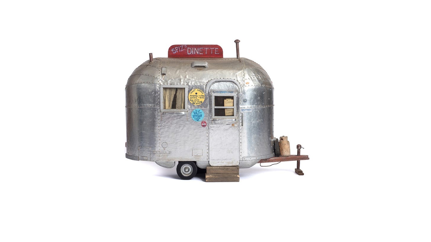 Spiz’s dinette, a toaster-size trailer with a propane tank no bigger than your thumb, was painstakingly crafted during Dean Gillispie’s years of incarceration at an Ohio prison. Gillispie constructed the silver trailer by spreading cigarette-pack foil across notebook cardboard, and used pins taken from the prison sewing shop to hold the whole structure together. The window curtains, made from used tea bags, are partially closed. A tiny sign on the trailer door reads, in nearly microscopic inky script: gone fishing. The whole sculpture invites you to lean closer, to peer through the tea-bag curtains and squint at the sign—only to encounter a message that is a declaration of absence, an ironic claiming of the very leisure time that prison makes impossible. Written from the claustrophobic quarters of a prison cell, the note turns a cliché of leisure into an act of fugitive self-possession.