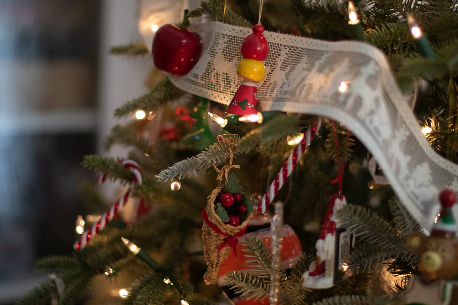 Close-up of the branches of a decorated Christmas tree. In the foreground are several wooden and rattan ornaments.