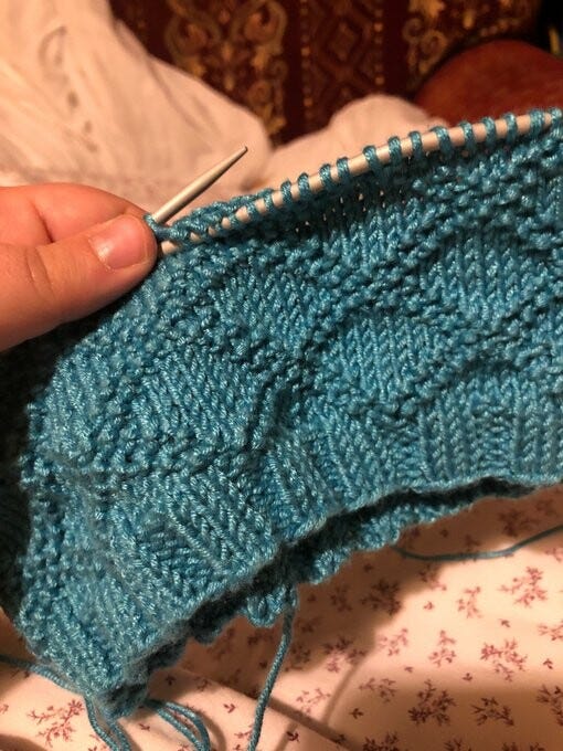 Knitting in progress: the first 3 or 4 inches or so of the hat I’m making. It’s in a deep turquoise yarn (sirdar baby bamboo, since you ask!) which has a nice gentle sheen to it. The knit is about an inch of ribbing (k3p3) and then a texture pattern called “King Charles brocade” (yuk) which is tesselating diamonds outlined in double-rows of purls. 
