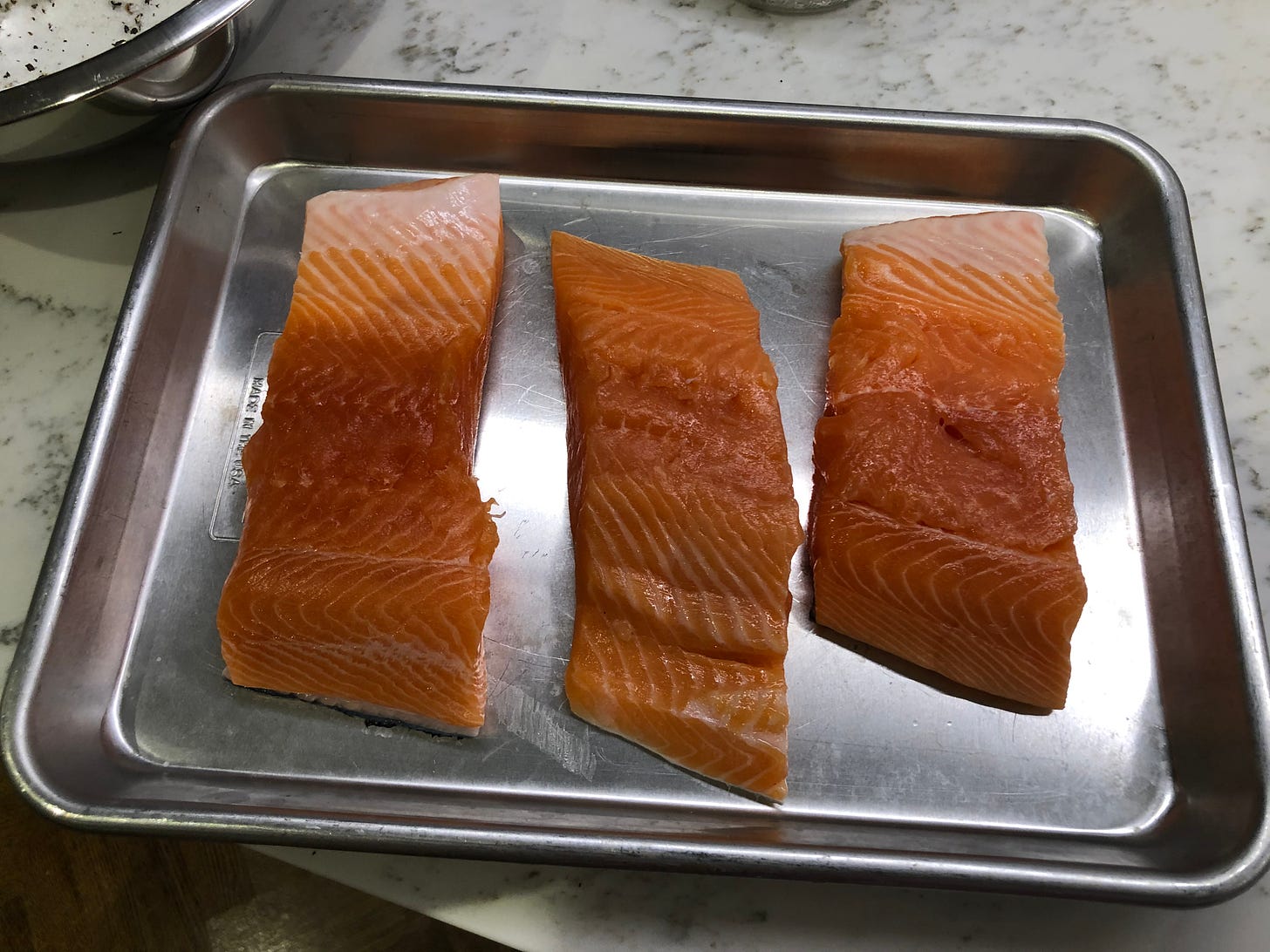 Three pieces of salmon on a metal tray