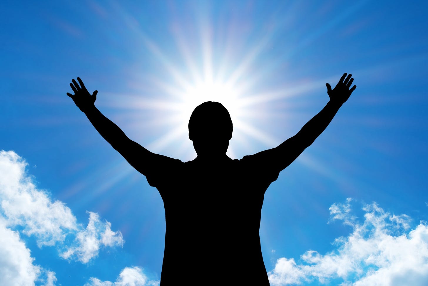 A person holds their hands up to the sky in a sign of worship. The sun shines above them like a halo.
