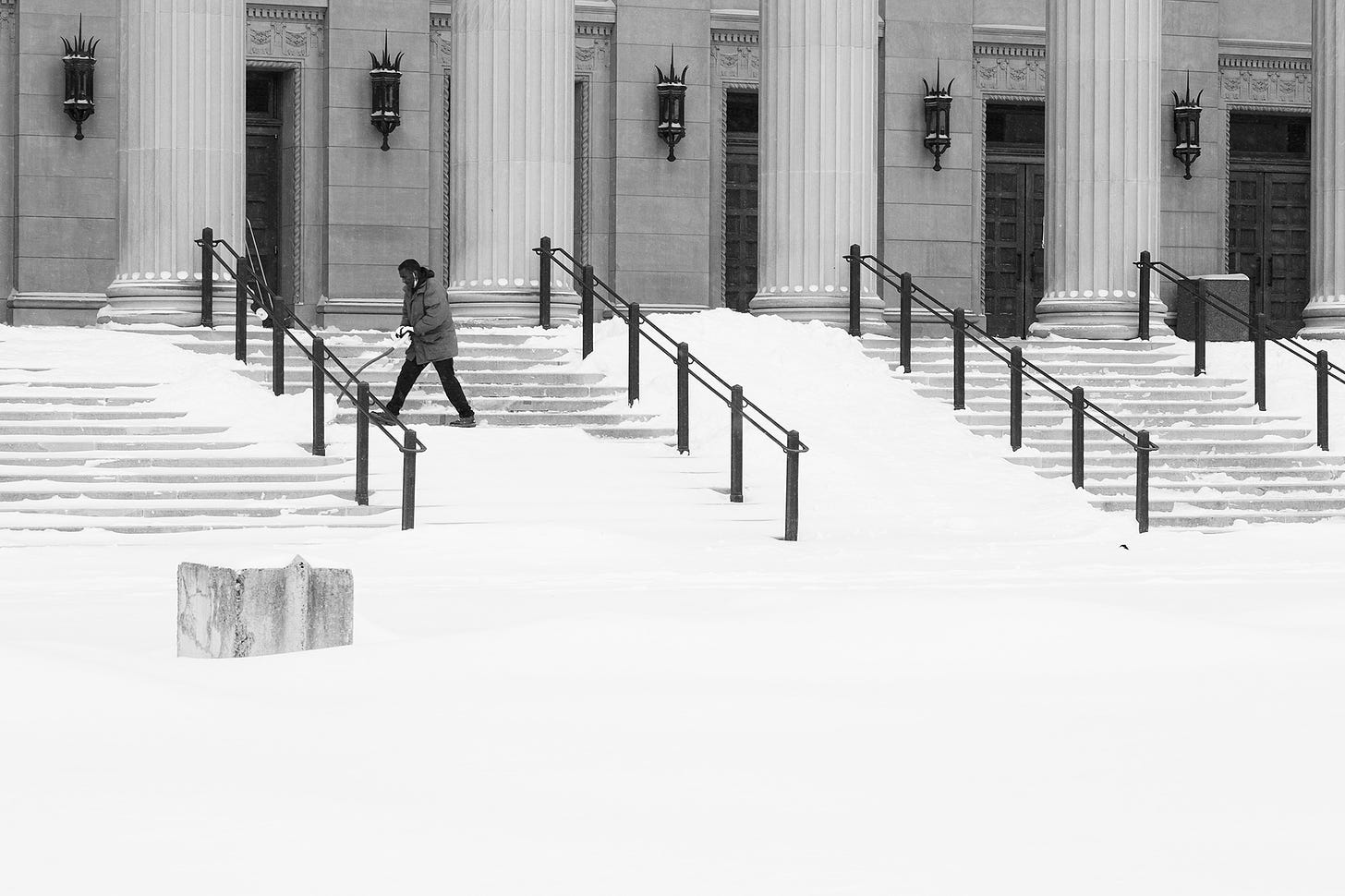 A man shovels snow from the main steps of the Northrop auditorium.