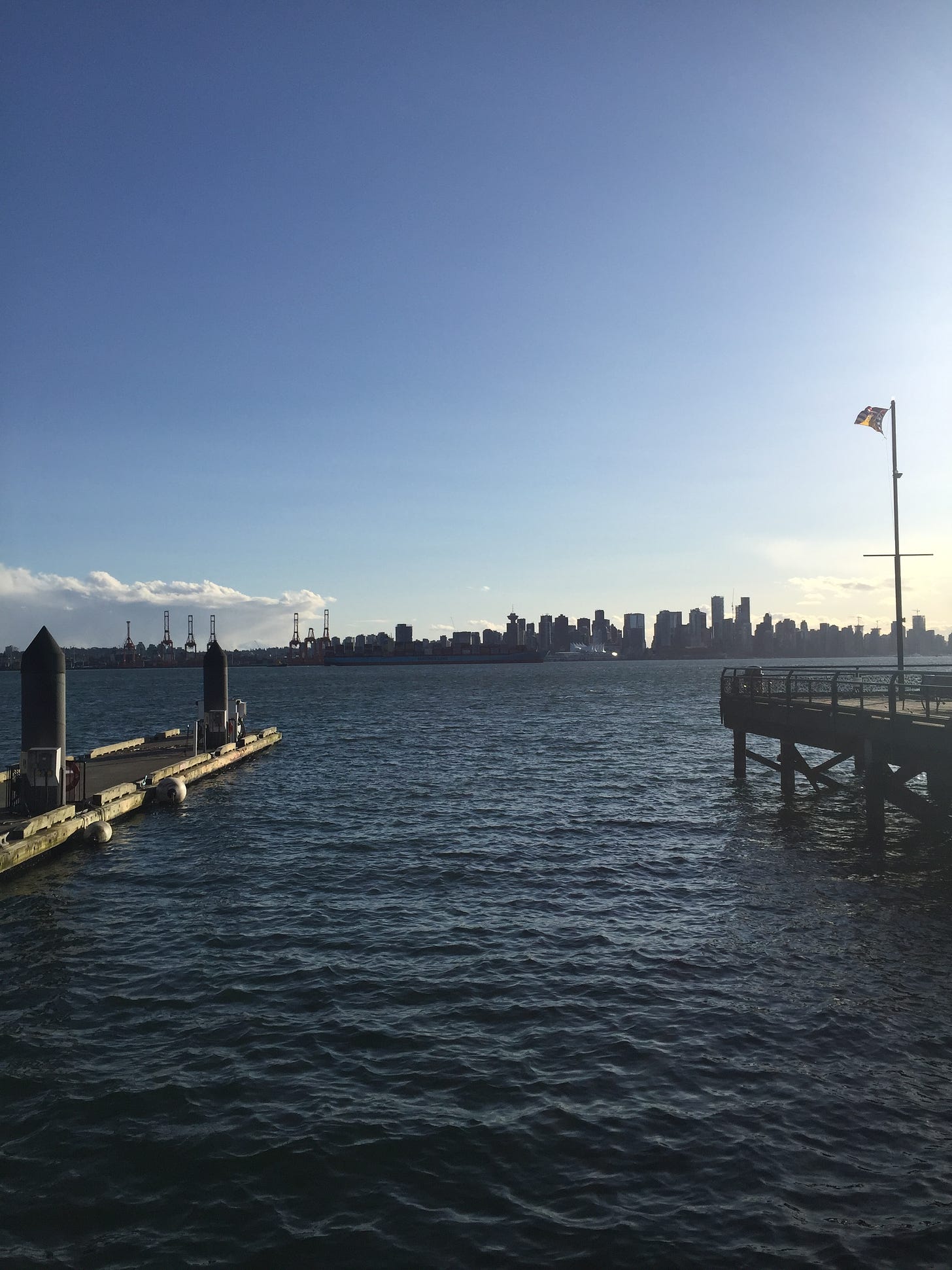 The Vancouver skyline, viewed across the water from the Shipyards area of Lonsdale. Corners of the pier are visible at either edge of the photo in the foreground.