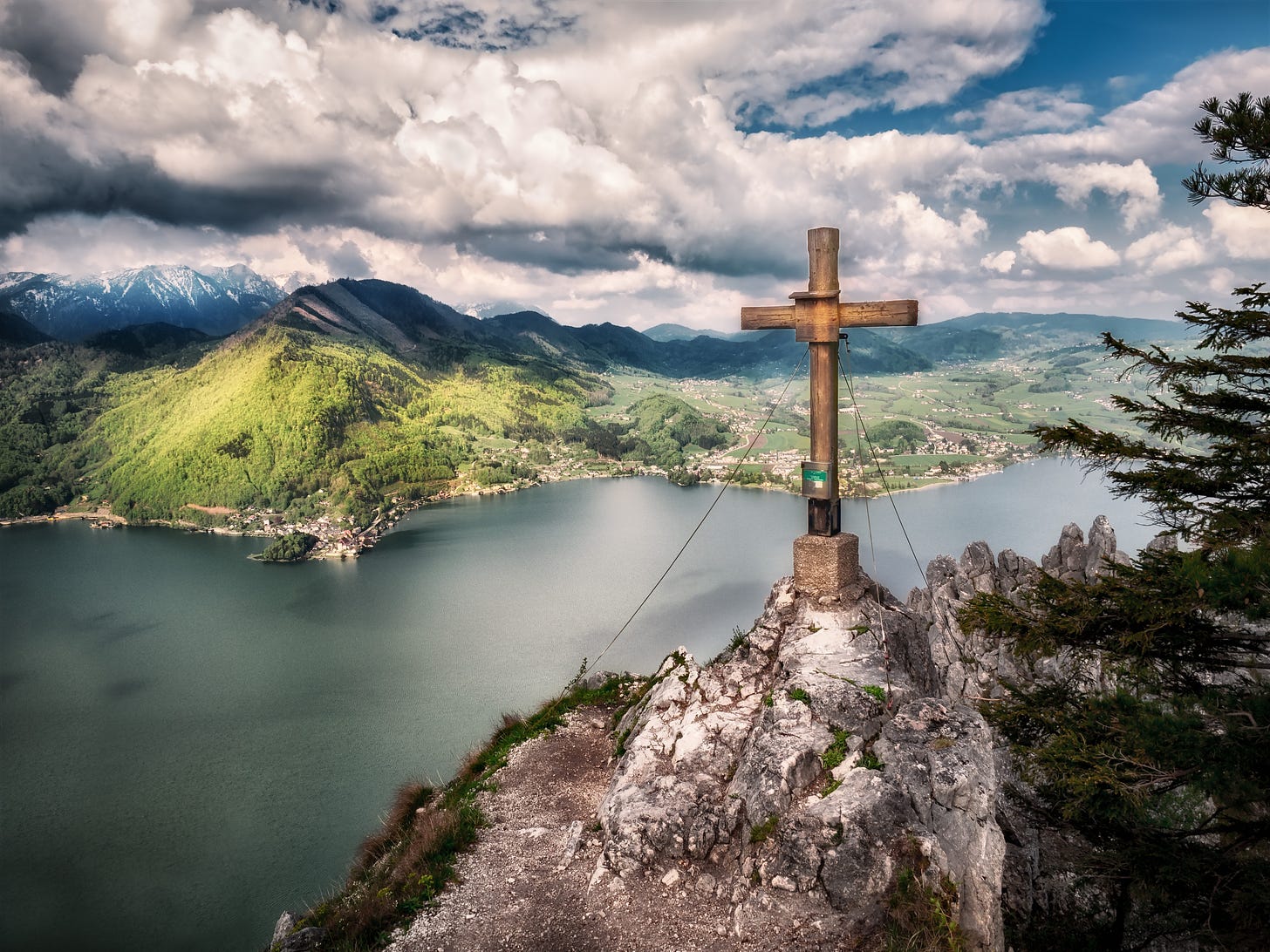 A cross on a mountain with rolling hills and a lake in the background.