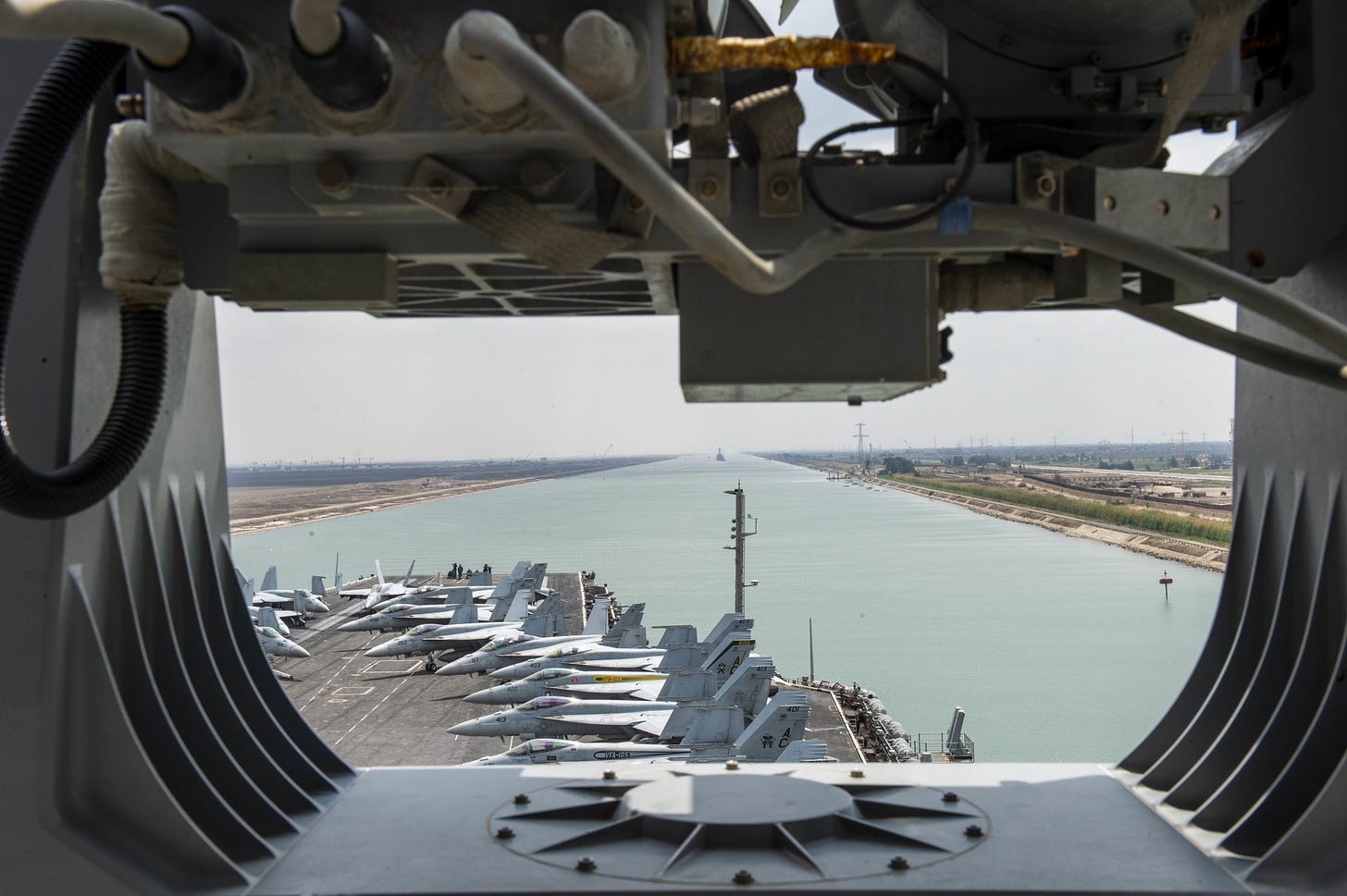 An aircraft carrier transits the Suez Canal. It has many planes on deck.