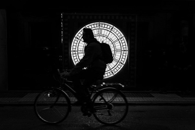Una silueta de un ciclista cruza delante de un reloj por la noche (Sevilla)
