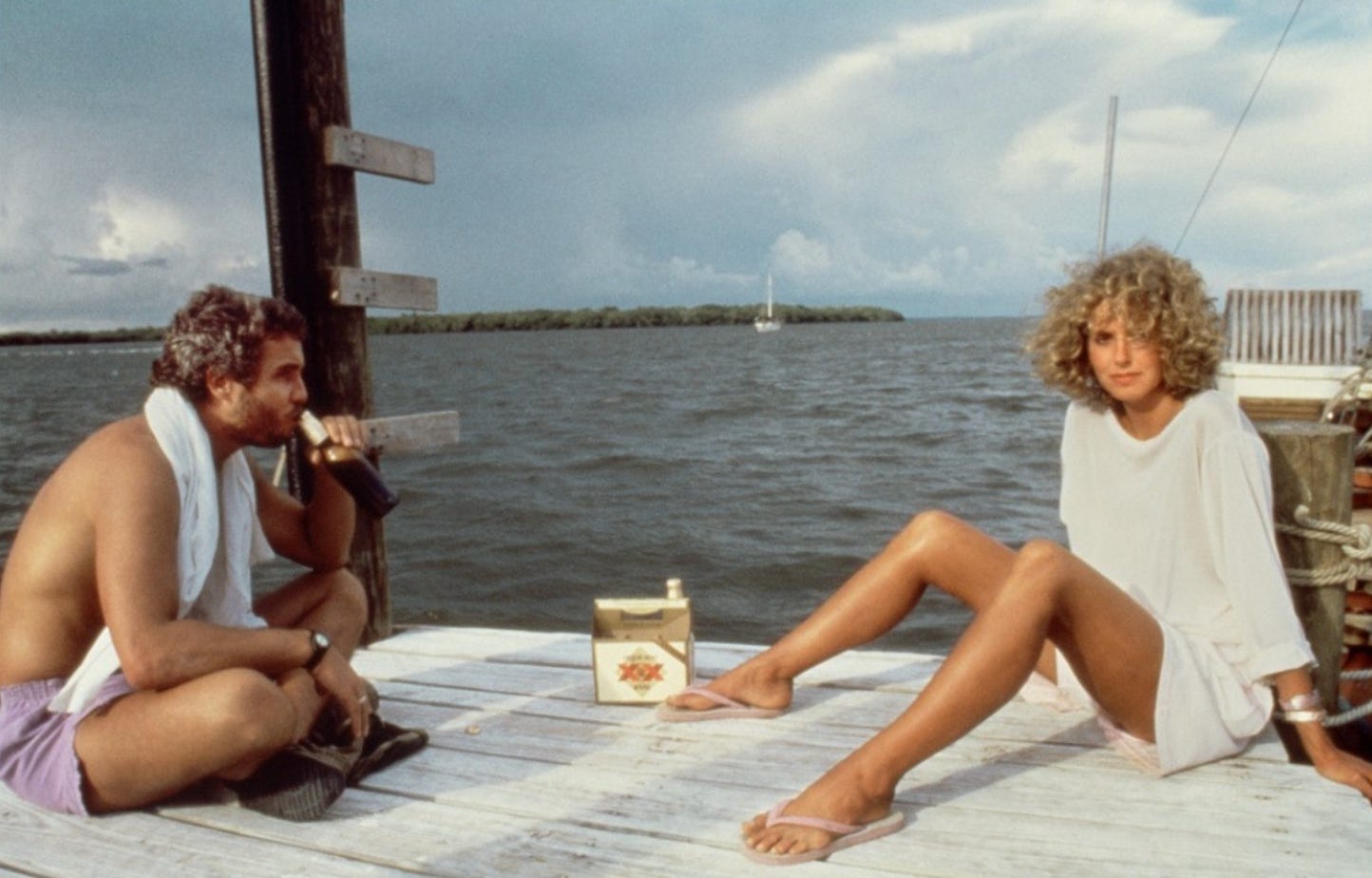 Screengrab of Will and Kim from Manhunter (1986). They're sitting on a dock on Marathon, Florida. Will is drinking a beer. Kim is looking at the camera.