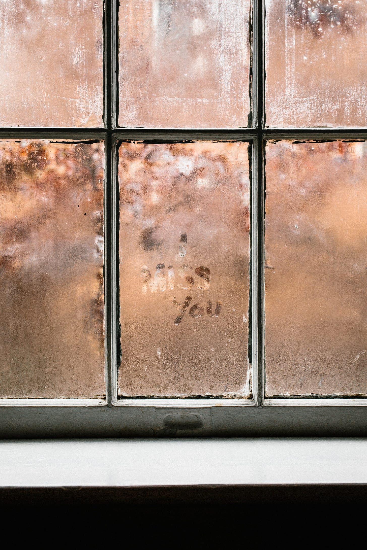 Water condensation on window panes with the words "I miss you" traced in the condensation.