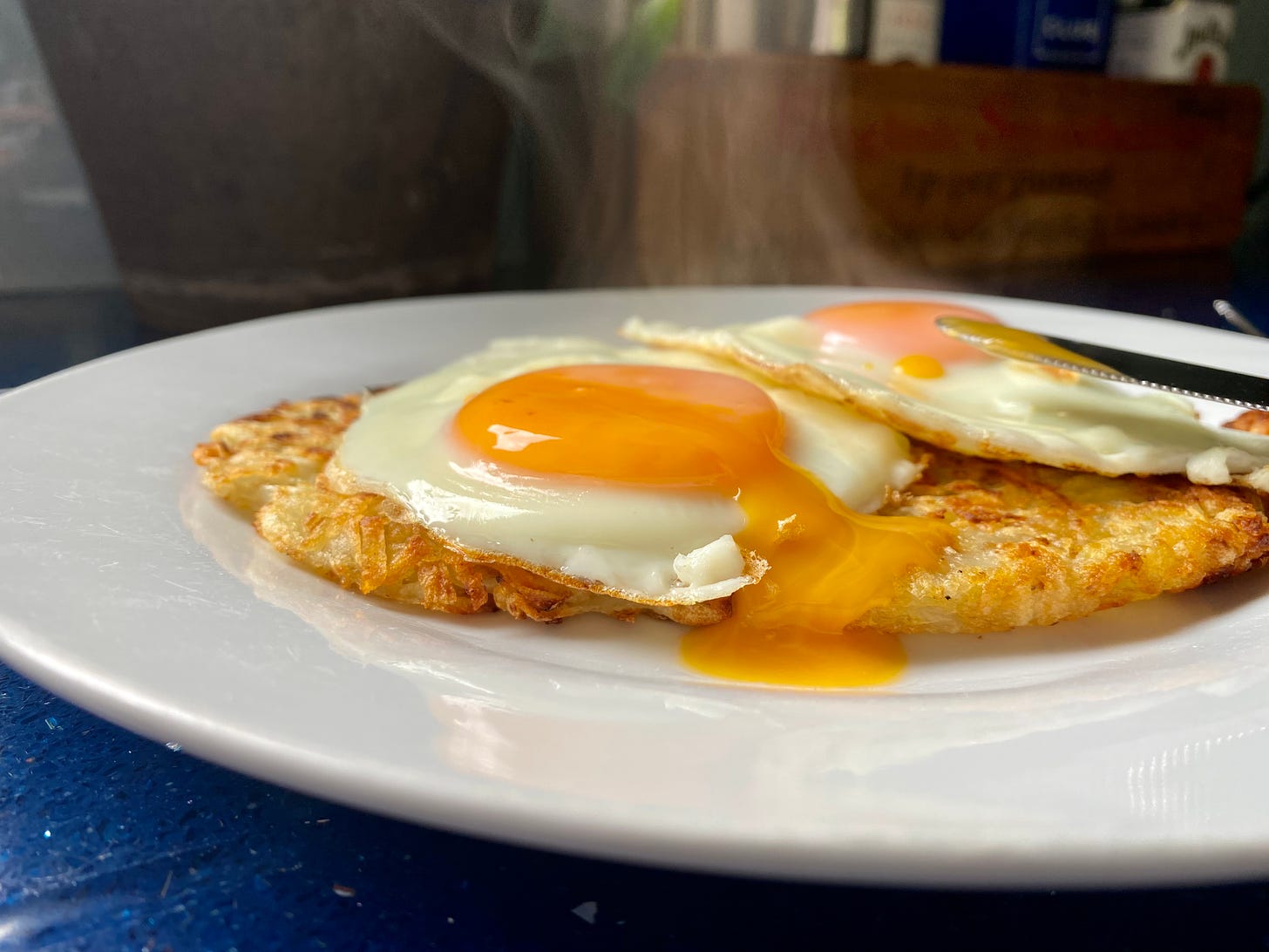 White plate holding potato rosti topped with runny yolk fried egg