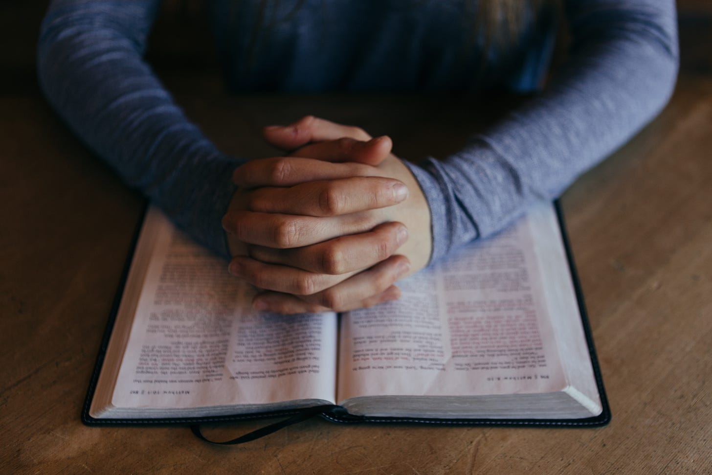 Clasped hands upon an open Bible as a gesture of praying