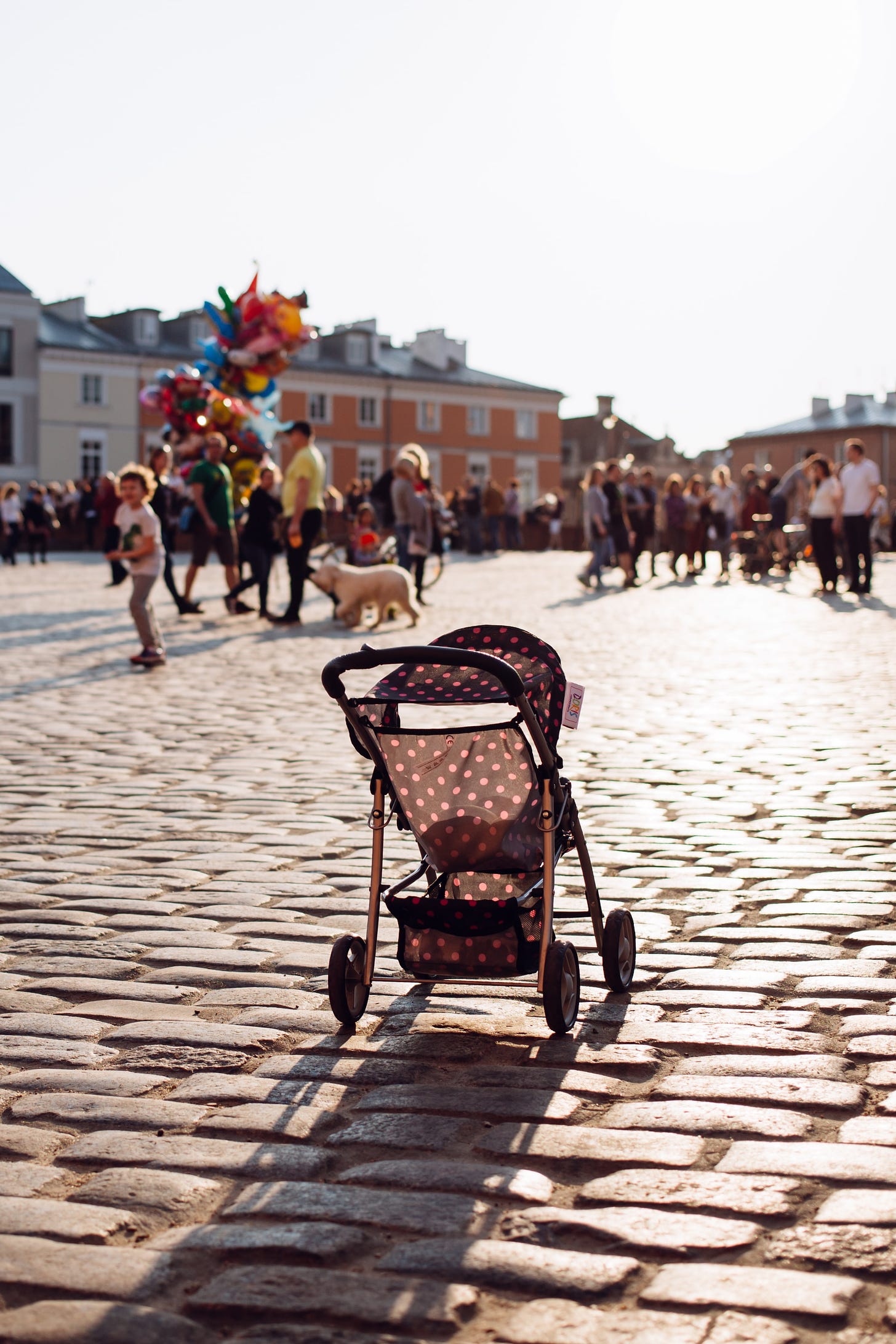 a polkadot-patterned baby stroller, empty, in the middle of a cobblestone square
