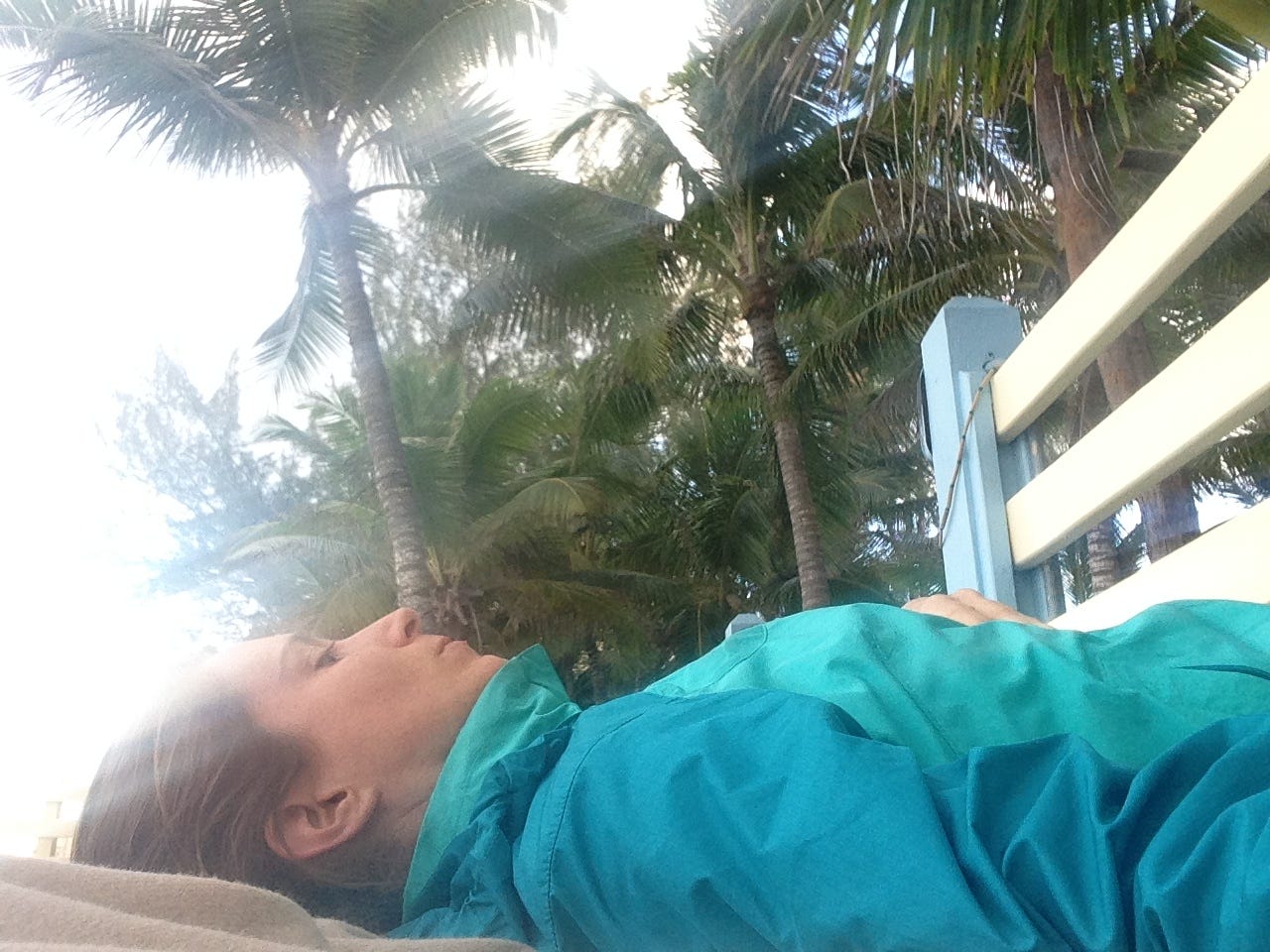 photo of author lying on the yoga platform with palm trees above her. she is wearing a jacket zipped all the way up