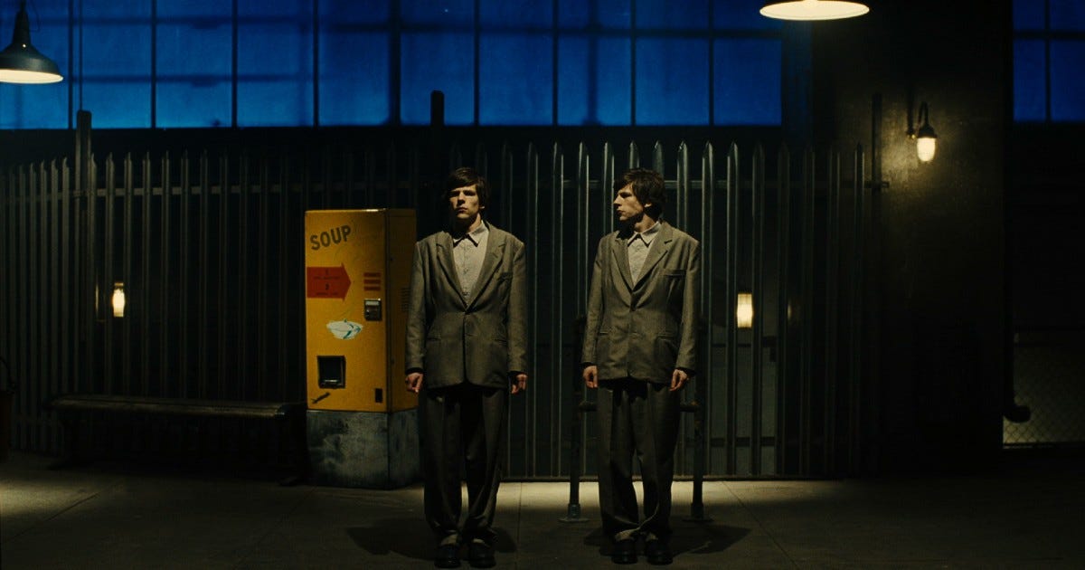 Movie still from The Double. Two identical men in business attire stand in a dimly lit hall.