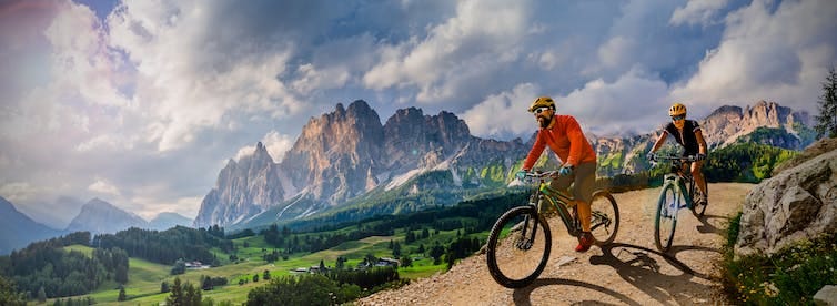 Woman and Man riding on bikes in Dolomites mountains landscape.