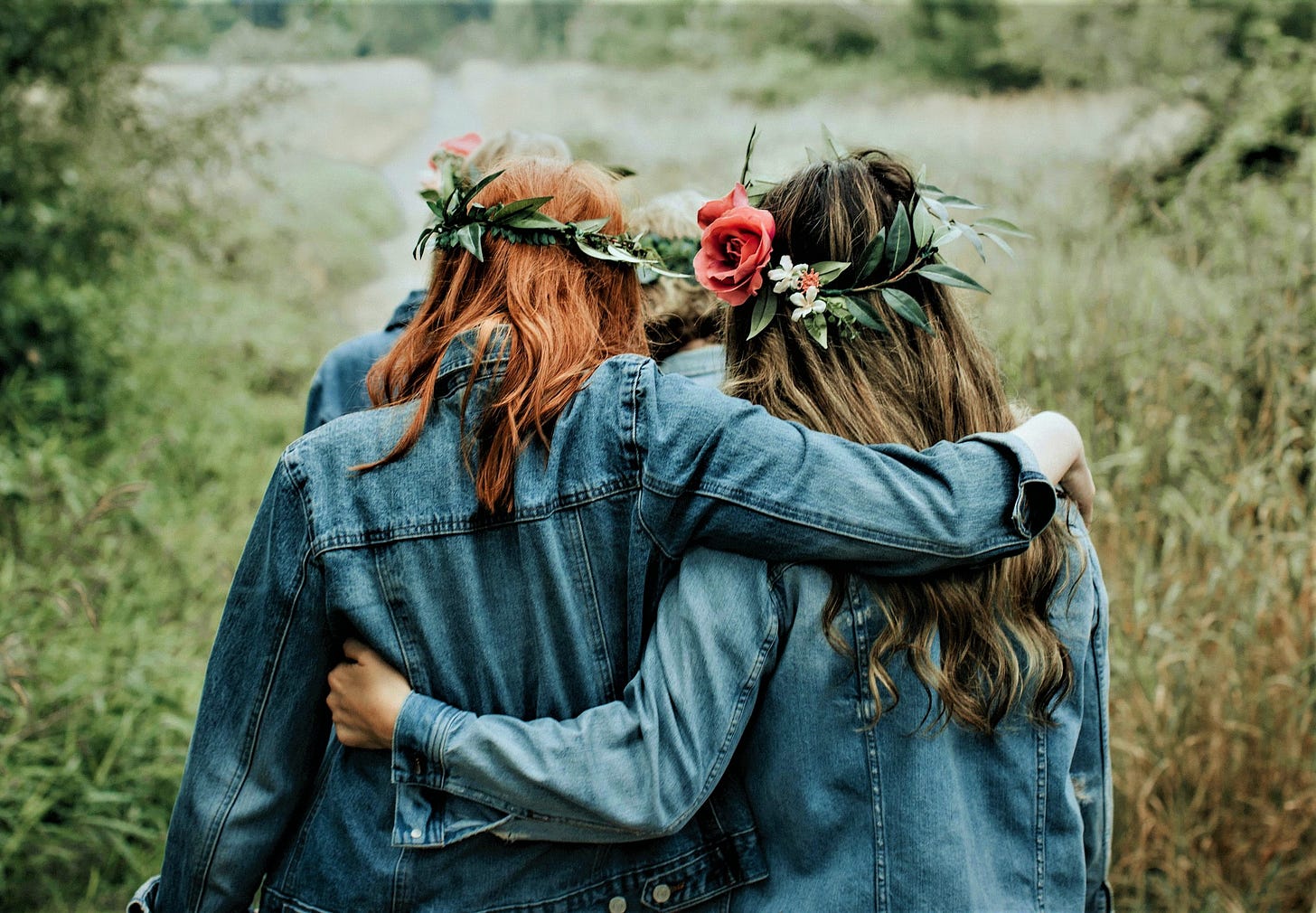 back view of two girls wearing denim jackets with flowers in their hair and arms around each other's waist