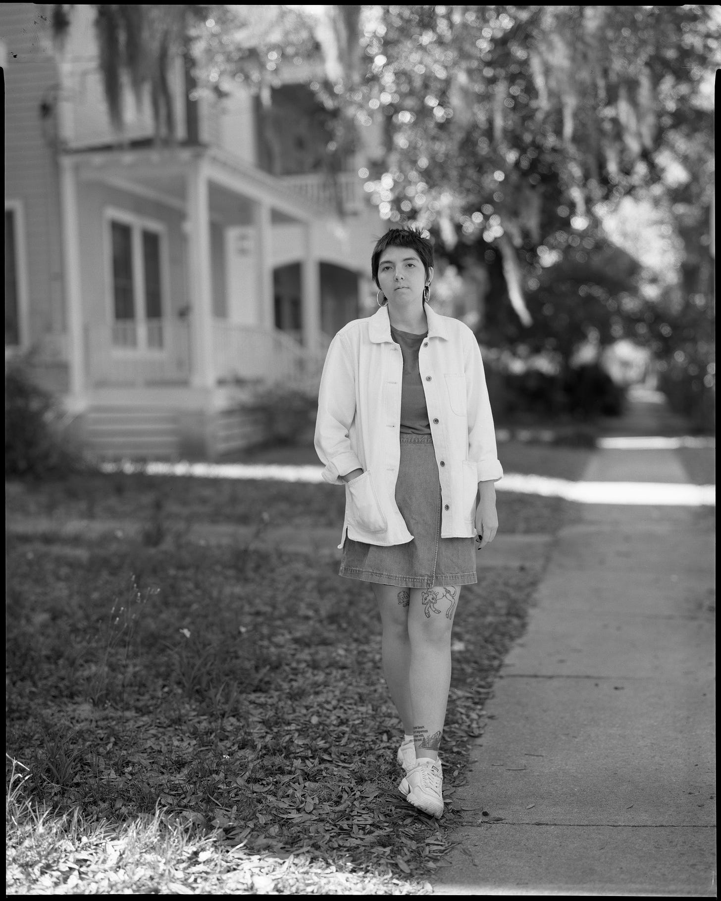 A young woman stands facing the camera with one hand in her pocket. As part of Portrait of US from the Nomadic Photo Ark