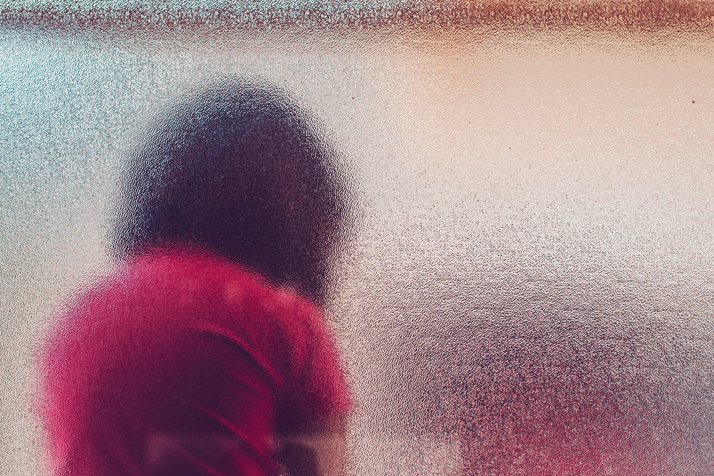 A child hangs their head sadly behind an opaque pane of glass.