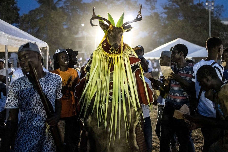 Several people gather at a rally; one wears a traditional costume topped with a deer mask.