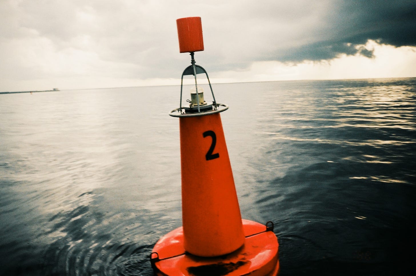 An orange marine buoy floats in a large body of water on a cloudy day