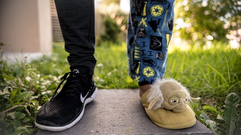 The bottom half of a man's legs, one dressed casually and the other in pajamas and a Yoda comfy slipper