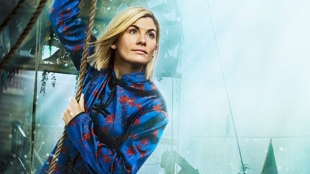 This image shows the Thirteenth Doctor (played by Jodie Whittaker) dressed in her colorful "Legend of the Sea Devils" costume and holding onto a rope as she prepares to swing from one Chinese pirate ship to another. This image shows the Thirteenth Doctor (played by Jodie Whittaker) dressed in her colorful "Legend of the Sea Devils" costume and holding onto a rope as she prepares to swing from one Chinese pirate ship to another.