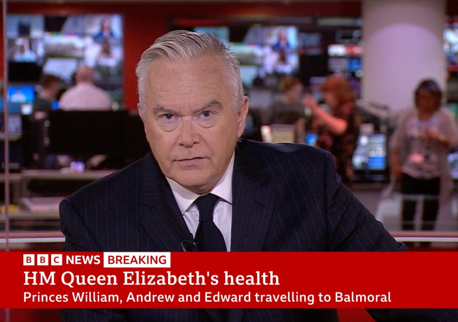 A news presenter in a black suit and tie.