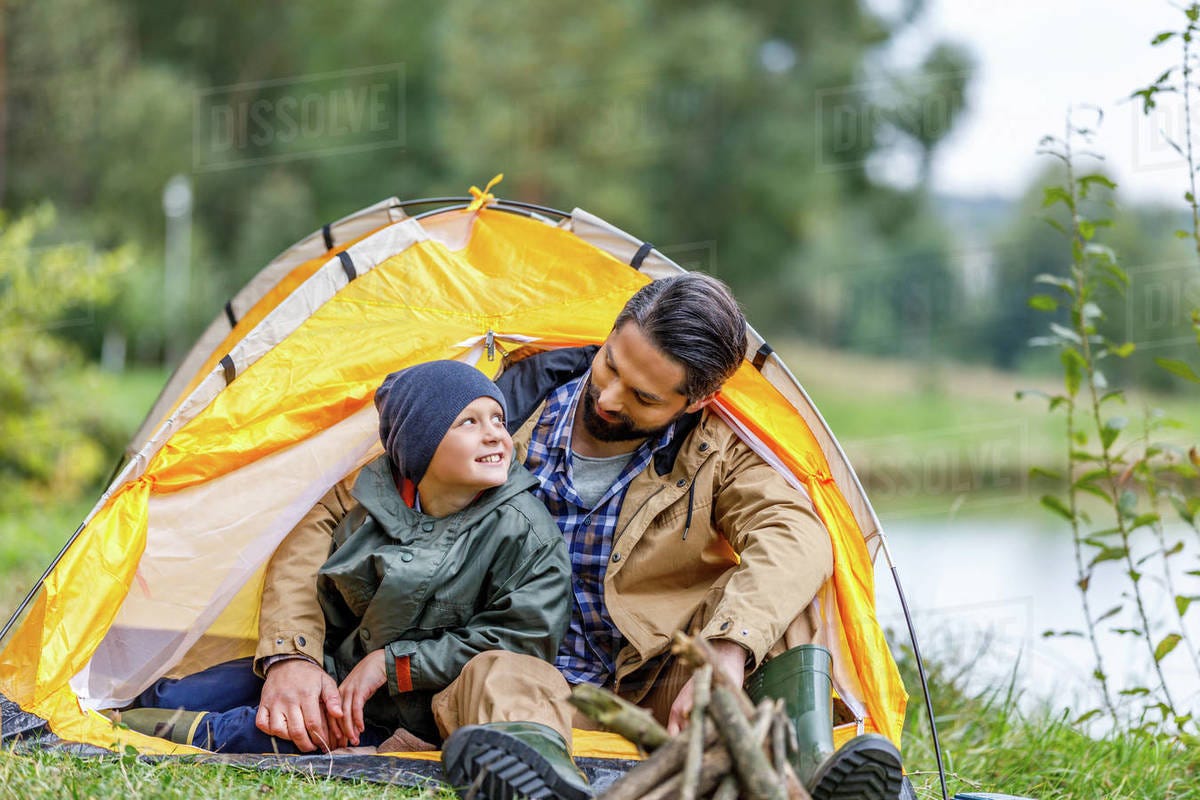 Happy father and son sitting in tent in camping at countryside - Stock  Photo - Dissolve
