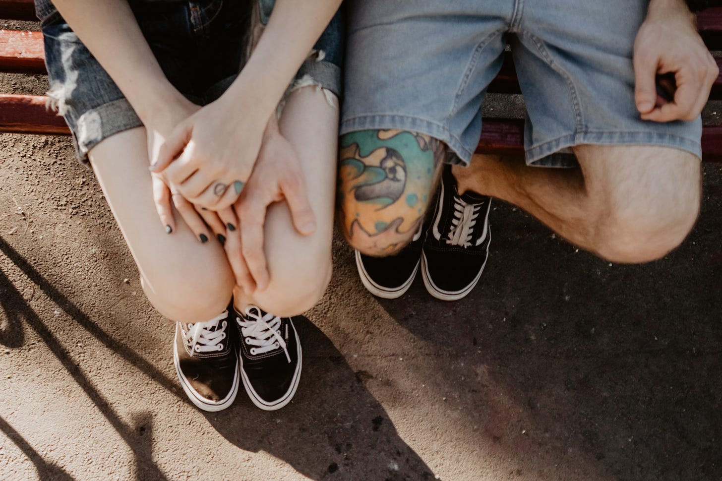 A couple with tattoos sit close to one another on a park bench.