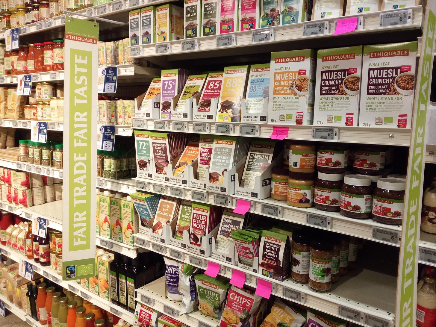 Supermarket aisle of Fairtrade-branded products under the banner 'Fair Trade Fair Taste.' Products include chocolate bars, tea, chocolate spread, spices and muesli.