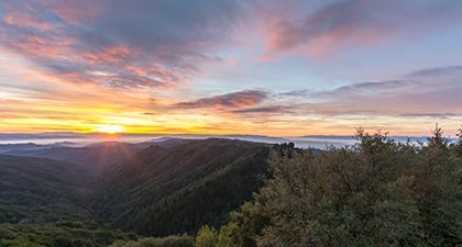 Colorful sunrise over dark forest-covered mountains