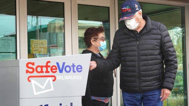 Residents drop mail-in ballots in an official ballot box outside of a Milwaukee library on Oct. 20, 2020.