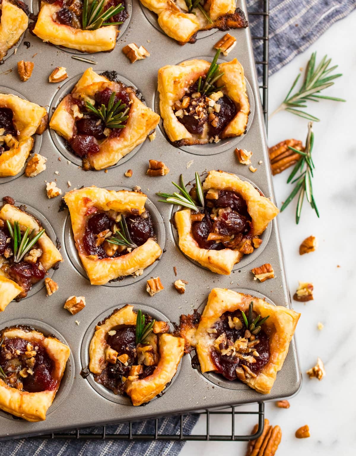 Delish cranberry brie bites in a mini muffin tin with pecans and fresh rosemary