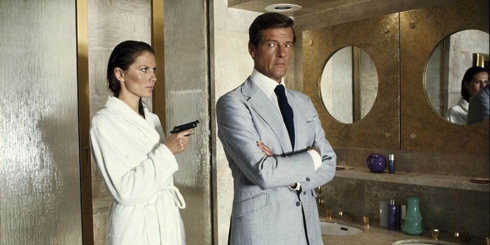 This image shows Andrea Anders (played by Maud Adams) dressed in a bathrobe and pointing a gun at James Bond (played by Roger Moore) in 1974's The Man with the Golden Gun. Andrea, who has just exited the shower of her Hong Kong Peninsula Hotel room, points her weapon at Bond's back, who stands in front of her with his arms crossed. This image shows Andrea Anders (played by Maud Adams) dressed in a bathrobe and pointing a gun at James Bond (played by Roger Moore) in 1974's The Man with the Golden Gun. Andrea, who has just exited the shower of her Hong Kong Peninsula Hotel room, points her weapon at Bond's back, who stands in front of her with his arms crossed.