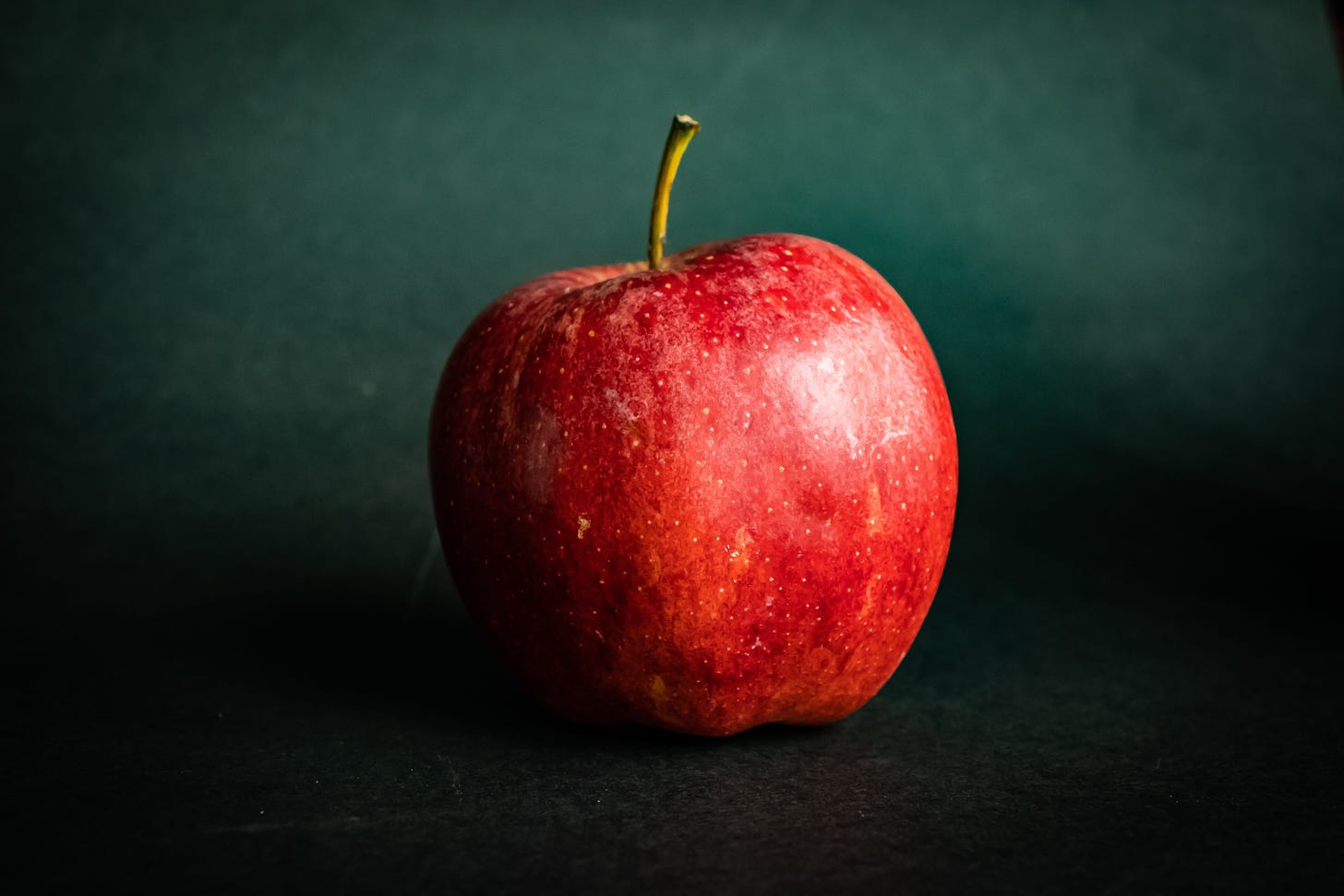 Photo of a red apple with  stem against a dark green backdrop.